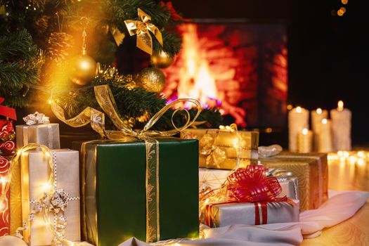 Stack of packed gift boxes under Christmas tree against burning fireplace. Lots of Christmas gifts under the tree. Candles on wooden floor. Focus on green box!