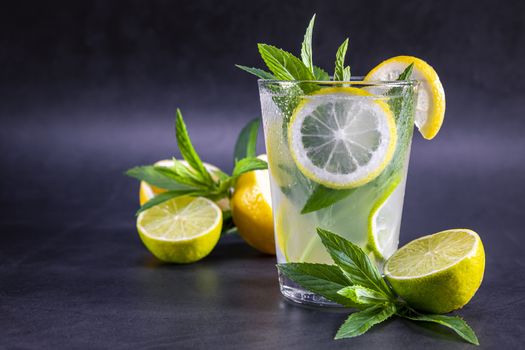 Cold refreshing summer lemonade with mint in a glass on a grey and black background. Focus on glass.