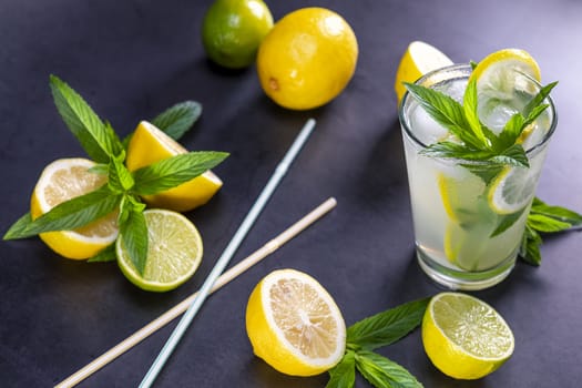 Cold refreshing summer lemonade with mint in a glass on a grey and black background. Focus on leaf in glass.