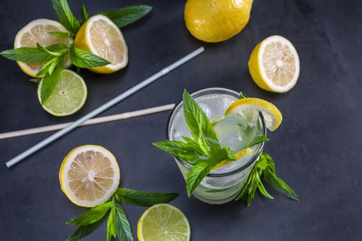 Cold refreshing summer lemonade with mint in a glass on a grey and black background. Focus on leaf in glass.