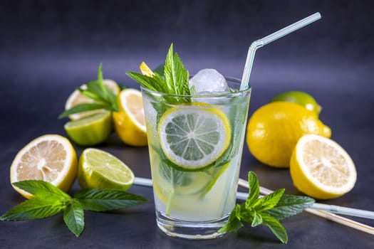 Cold refreshing summer lemonade with mint in a glass on a grey and black background. Focus on leaf and ice in glass.