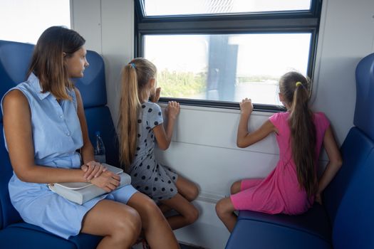 Mom and two daughters ride in an electric train, children look out the window