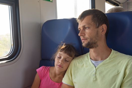 Girl sleeping leaning on dad's shoulder in an electric train car