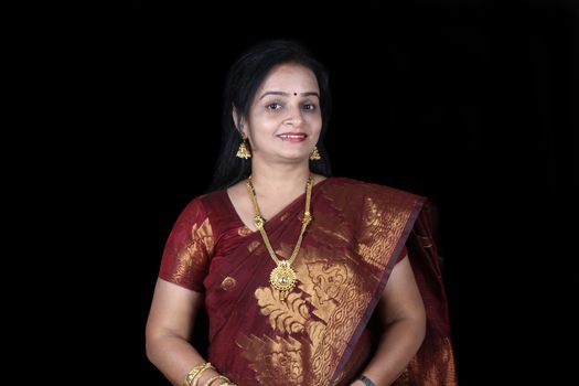 A smiling middleaged Indian woman in a traditional saree, on black studio background.