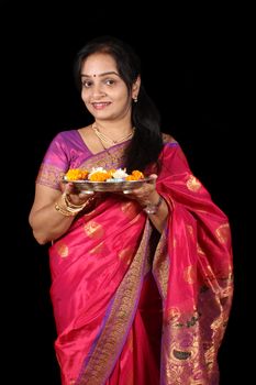 A beautiful Indian Indian woman holding a hindu ritual plate, on black studio background.