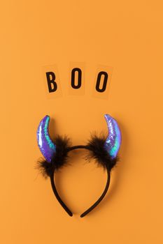 Halloween holiday flat lay. Party accessory, rim with devil horns and inscription Boo on orange background, copy space. Minimal style. Vertical. Trick-or-treat concept.