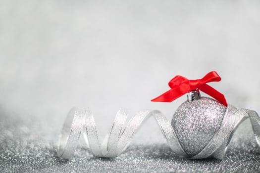 Christmas holiday composition of festive decor ball with red ribbon bow on silver glitter bokeh background