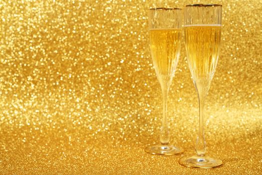 Two glasses of champagne with golden glitter lights on background