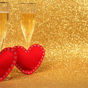 Two glasses of champagne and red hearts with golden glitter lights on background