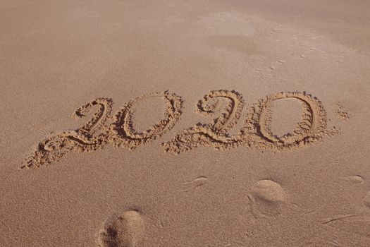 Happy New Year 2020, lettering on the beach. Numbers 2020 year on the sea shore, message handwritten in the golden sand on beautiful beach background. New Years concept.