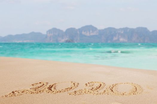 Happy New Year 2020, lettering on the beach. Numbers 2020 year on the sea shore, message handwritten in the golden sand on beautiful beach background. New Years concept.