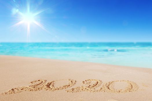 Happy New Year 2020, lettering on the beach. Numbers 2020 year on the sea shore, message handwritten in the golden sand on beautiful beach background. New Years concept.