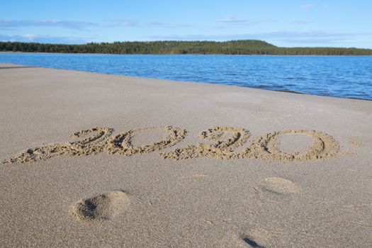 Happy New Year 2020, lettering on the beach. Numbers 2020 year on the sea shore, message handwritten in the golden sand on beautiful beach background. New Years concept.