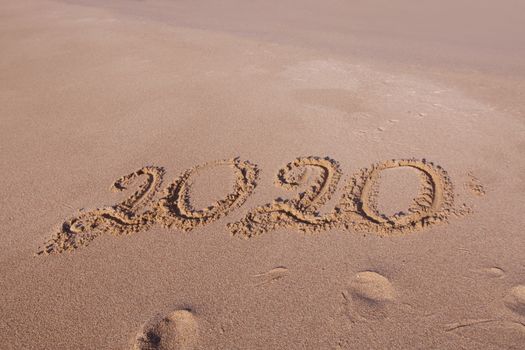 Happy New Year 2020, lettering on the beach. Numbers 2020 year on the sea shore, message handwritten in the golden sand on beautiful beach background. New Years concept.