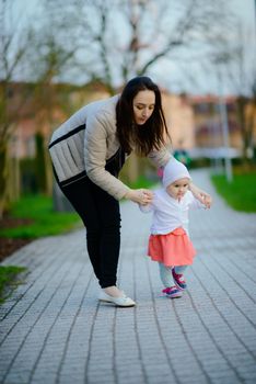 Happy mother holds her daughter's hands and teaches her how to walk. first steps. learning to walk. authentic motherhood. Happiness and harmony in family life