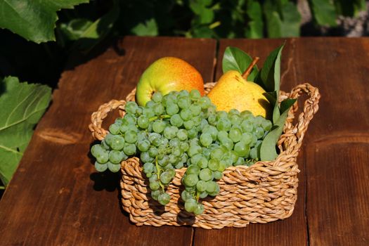 The picture shows a basket mit delicious fruits on wooden boards.