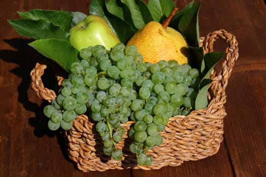 The picture shows a basket mit delicious fruits on wooden boards.