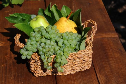 The picture shows a basket mit delicious fruits on wooden boards.