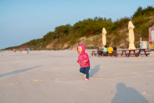 Adorable toddler girl on a sunny sand beach. Authentic childhood