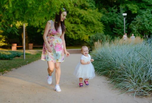 Happy mother and daughter in the park. Beauty nature scene with family outdoor lifestyle. Happy family resting together on the green grass, having fun outdoor. Happiness and harmony in family life.