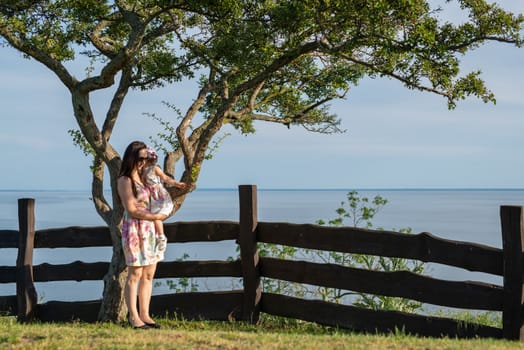 Happy mother and daughter in the park. Beauty nature scene with family outdoor lifestyle. Happy family resting together on the green grass, having fun outdoor. Happiness and harmony in family life.