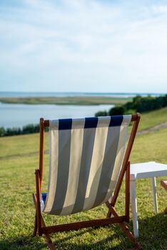 Empty beach chair on meadow on summer time. Sunlight and sea in the background. Coast line