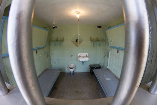 Prison bars in the forground with uncomfortable prison beds in the background