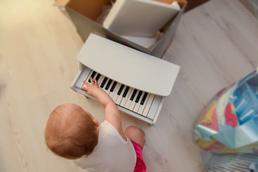 beautiful baby girl playing toy piano in light room. Authentic image.