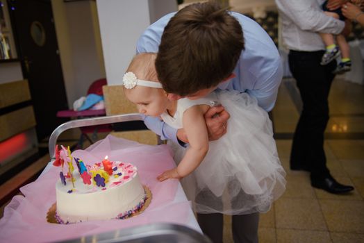 Baby girl 1 year old eating birthday cake in room. Birthday party. Childhood.