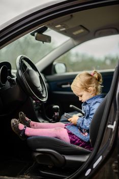 Little girl in a car seat. Holding phone in her hand. Taking driver seat. Car damage. Authentic image.