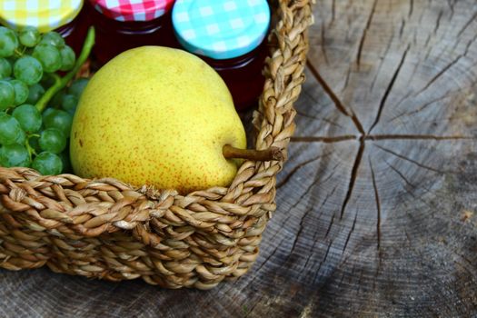 The picture shows a basket with fruits and jelly on wooden ground.