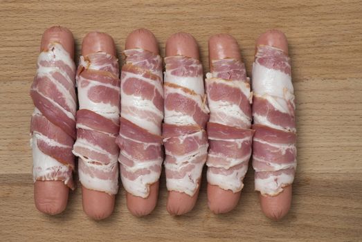 Preparation of raw sausages wrapped spirally in bacon on a wooden background. Top view.