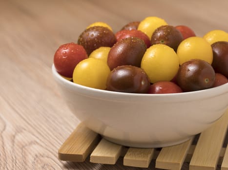 Cherry tomatoes in a variety of colors in ceramic bowl on wooden background.