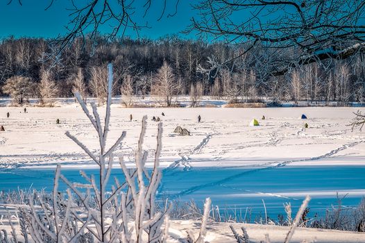 Winter landscape with a lake and fishermen on the ice.