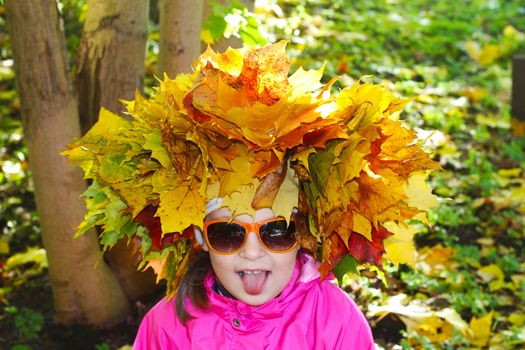 
Autumn wreath on the head of a girl in black glasses on a background of green and yellow leaves.