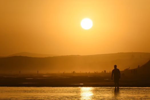 A man watches as the sun nears the horizon on a summer vacation beach, Mossel Bay, South Africa