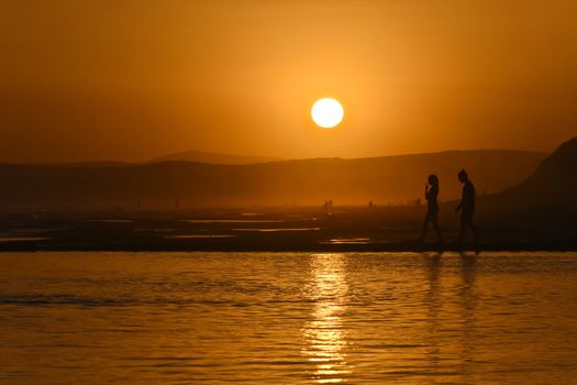 Two young lovers walking on the edge of a tide pool before the sunset, Mossel Bay, South Africa