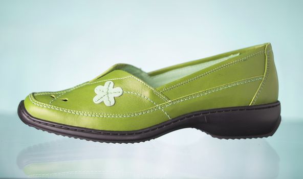 Female green leather shoe on green background, isolated product.