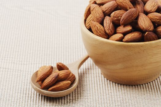 Close of dry almonds nuts in a wooden spoon over corrugated paper background.