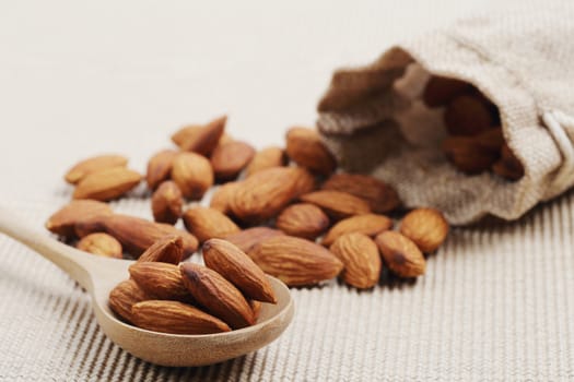 Close of dry almonds nuts in a wooden spoon over corrugated paper background.