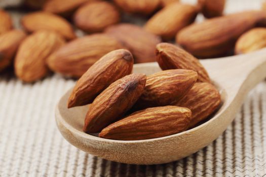 Close of dry almonds nuts in a wooden spoon over corrugated paper background.