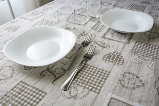 Table set with plates, glasses, cutlery and tablecloth. Interior shot