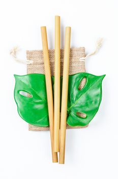 Biodegradable bamboo straws with burlap bag and green leaf on white background. Eco concept. Packaging straws made of bamboo.