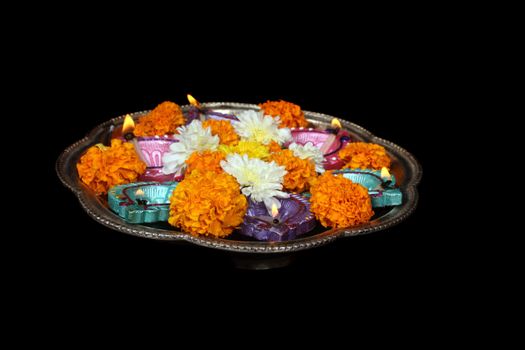 A holy plate containing flowers and lamps for a traditional Diwali ritual, on black studio background.