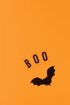 Halloween holiday flat lay. Black plastic bat and inscription Boo on orange background, copy space. Minimal style. Vertical. Trick-or-treat concept.