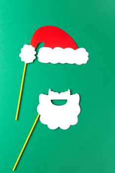 Christmas decoration, white beard and red Santas hat on sticks. Festive concept, party accessories. Vertical, flat lay. Minimal style. Top view.