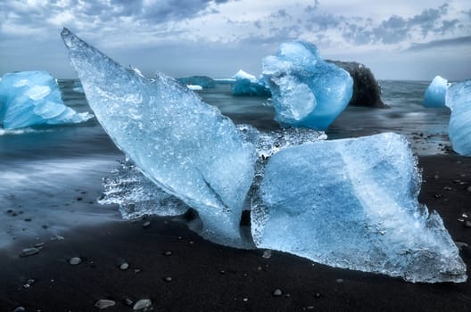 Ice-blocks looking like a whale's tail with black sand and smooth water at Diamond Beach, Iceland