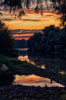 River at sunset with little lake, rocks and leaves in the foreground