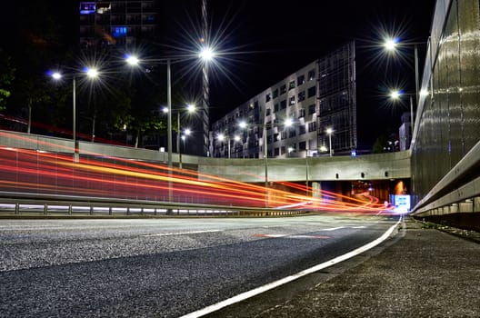 Tunnel opening in city with car trails surrounded by asphalt and concrete with modern buildings