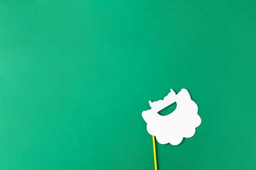 Christmas decoration, white Santas beard on stick on green background with copy space. Festive concept, party accessories. Horizontal, flat lay. Minimal style. Top view.